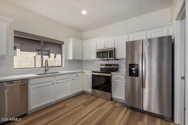 kitchen with stainless steel appliances, white cabinets, sink, decorative backsplash, and hardwood / wood-style flooring