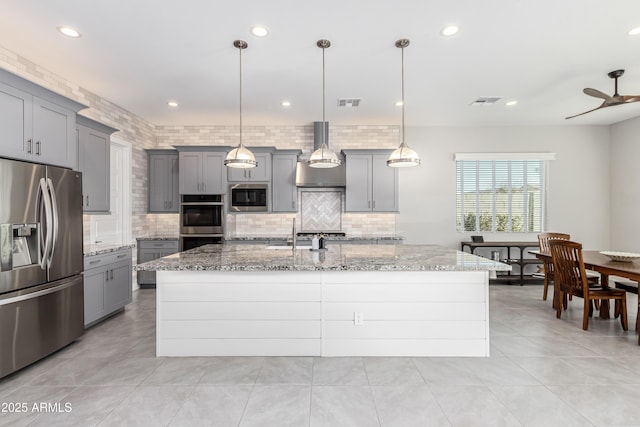 kitchen featuring light stone counters, decorative light fixtures, an island with sink, and appliances with stainless steel finishes