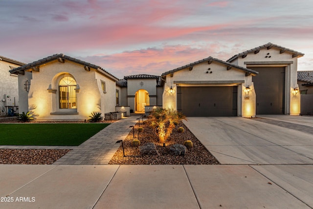 mediterranean / spanish house with an attached garage, a tiled roof, concrete driveway, and stucco siding