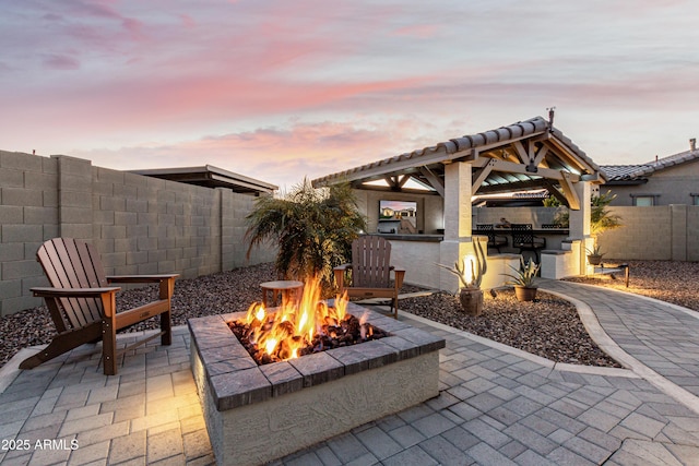 patio terrace at dusk featuring a gazebo, an outdoor kitchen, and a fire pit