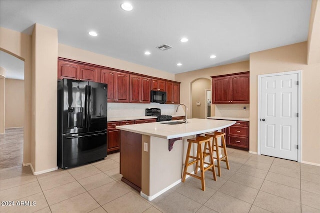 kitchen featuring sink, a kitchen breakfast bar, an island with sink, light tile patterned floors, and black appliances