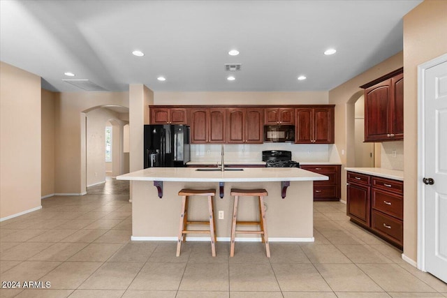 kitchen featuring sink, an island with sink, a kitchen bar, light tile patterned floors, and black appliances