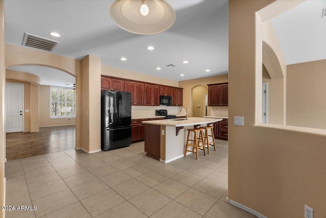 kitchen with sink, black appliances, light tile patterned floors, a breakfast bar area, and an island with sink