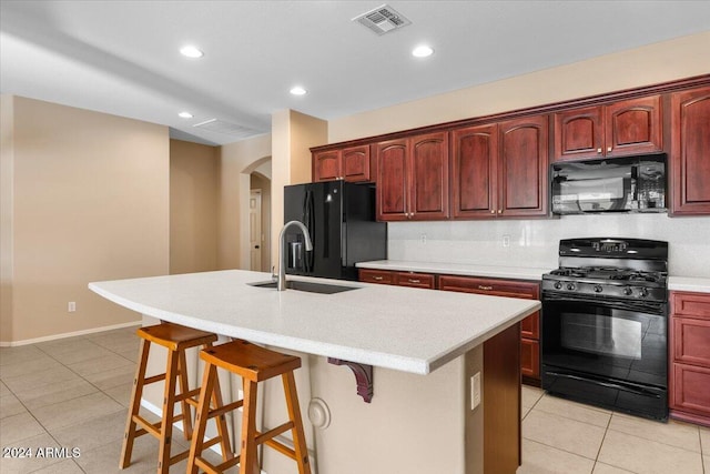 kitchen featuring sink, an island with sink, a kitchen bar, light tile patterned floors, and black appliances