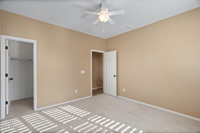 unfurnished bedroom featuring ceiling fan, a walk in closet, light carpet, and a closet