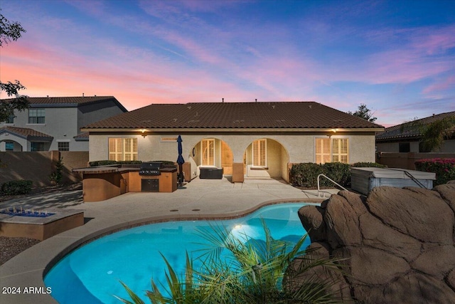 pool at dusk featuring a fire pit, an outdoor kitchen, and a patio area