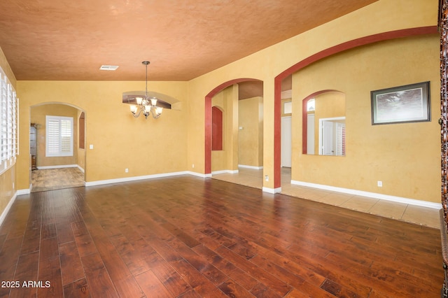 empty room with dark hardwood / wood-style floors and an inviting chandelier