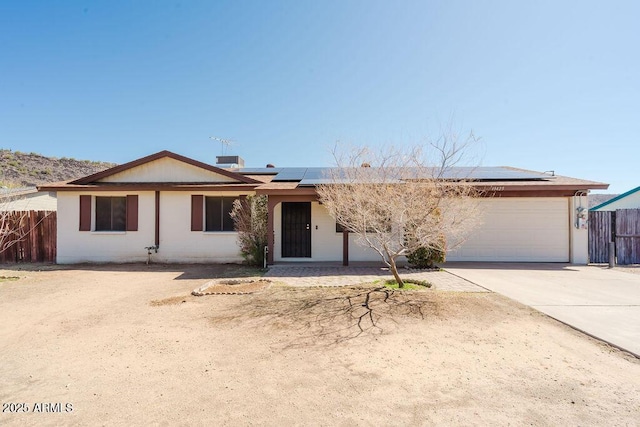 single story home featuring solar panels, concrete driveway, an attached garage, and fence