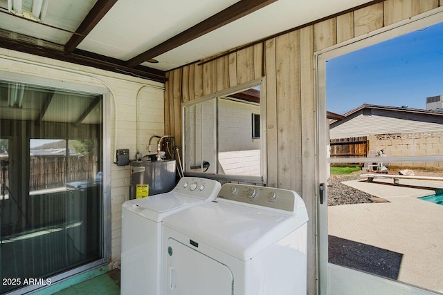 laundry area featuring laundry area, wood walls, electric water heater, and washing machine and clothes dryer