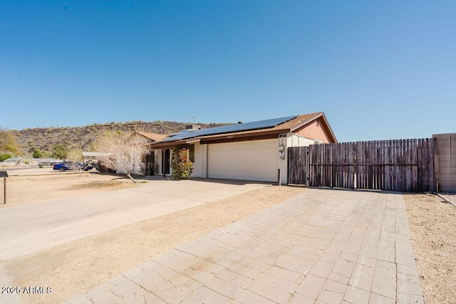 ranch-style home with roof mounted solar panels, concrete driveway, a garage, and fence