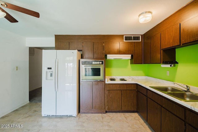 kitchen featuring white appliances, visible vents, a sink, light countertops, and under cabinet range hood