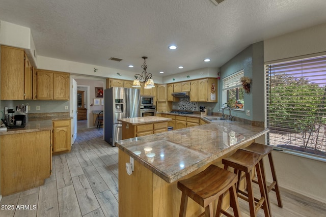 kitchen featuring a sink, a textured ceiling, light wood-type flooring, and appliances with stainless steel finishes