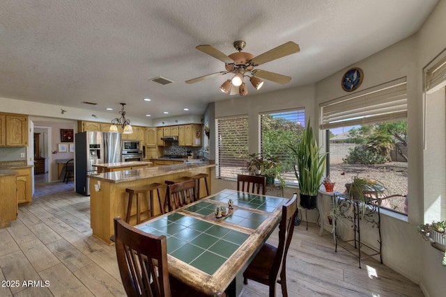 dining room with light wood-type flooring, visible vents, a ceiling fan, and a textured ceiling