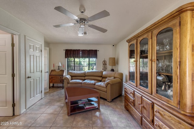 living area with a textured ceiling, light tile patterned flooring, and ceiling fan