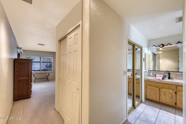 hallway with a textured wall, visible vents, and a sink