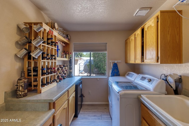 washroom featuring light wood-style flooring, a sink, cabinet space, a textured ceiling, and independent washer and dryer