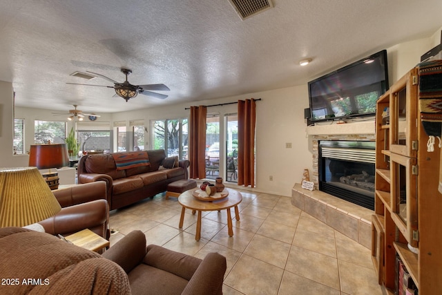 living area featuring light tile patterned floors, a fireplace, a textured ceiling, visible vents, and ceiling fan