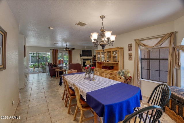 dining space with baseboards, visible vents, light tile patterned flooring, ceiling fan with notable chandelier, and a fireplace