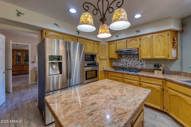 kitchen with under cabinet range hood, decorative light fixtures, decorative backsplash, stainless steel appliances, and light wood-type flooring