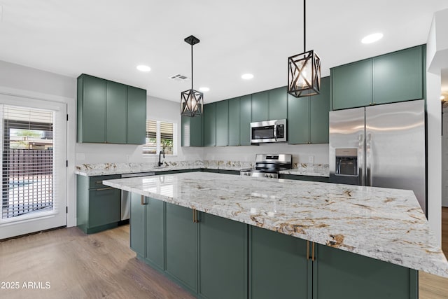 3607 N 79th Ave, Phoenix, AZ 85033 - kitchen with stainless steel appliances, green cabinets, light wood-style floors, light stone countertops, and hanging light fixtures