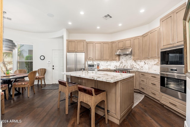 kitchen with backsplash, a center island with sink, dark hardwood / wood-style floors, light stone counters, and stainless steel refrigerator