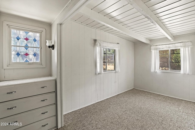 unfurnished bedroom with carpet flooring, beamed ceiling, multiple windows, and wooden walls