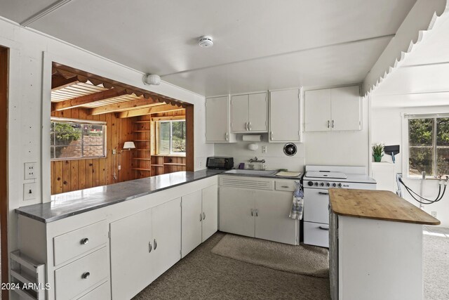 kitchen featuring white cabinetry, dark carpet, wood walls, gas range gas stove, and sink