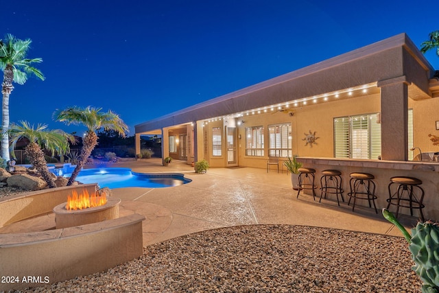 pool at twilight with outdoor dry bar, a patio, a fire pit, and an outdoor pool