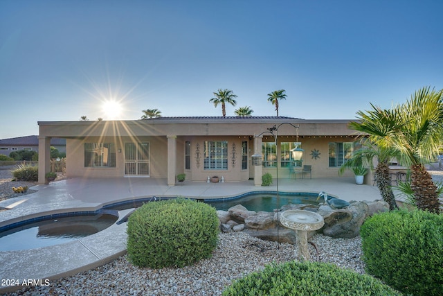 rear view of house featuring a patio, a pool with connected hot tub, and stucco siding