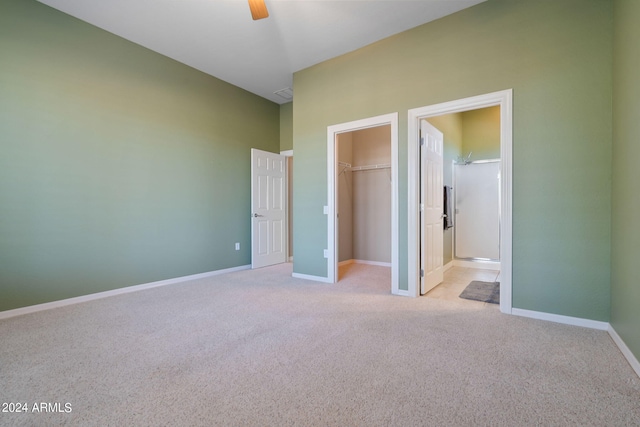 unfurnished bedroom featuring connected bathroom, ceiling fan, a closet, a walk in closet, and light colored carpet