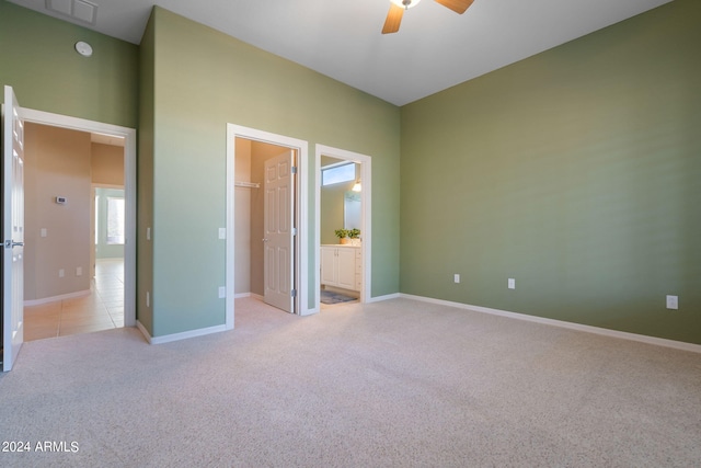 unfurnished bedroom with ceiling fan, connected bathroom, light carpet, and a spacious closet