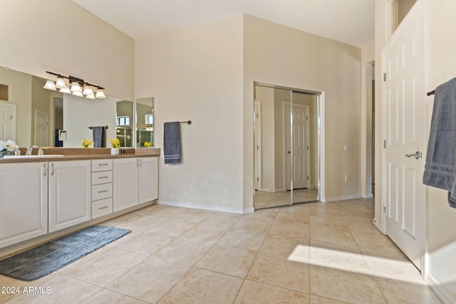 full bath with double vanity, a towering ceiling, a sink, tile patterned flooring, and baseboards