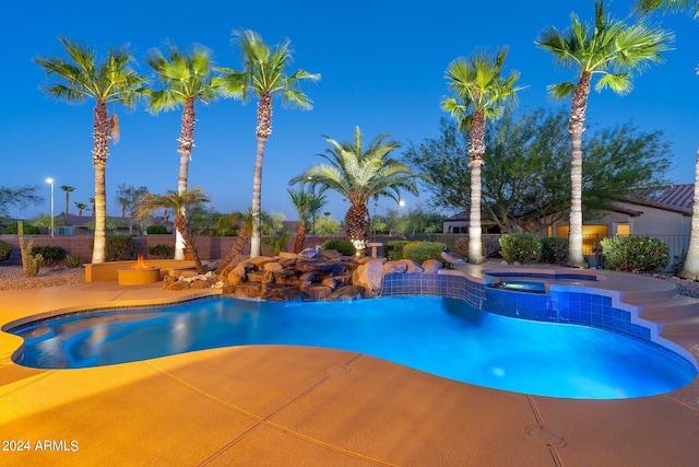 pool at twilight with a patio area and an in ground hot tub