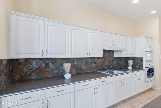 kitchen with white appliances, tasteful backsplash, light tile patterned floors, white cabinets, and under cabinet range hood