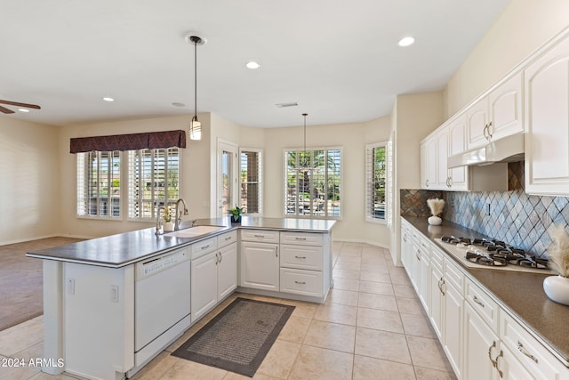 kitchen with dark countertops, decorative backsplash, a sink, white appliances, and under cabinet range hood