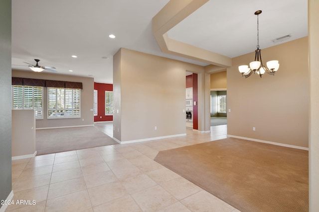 carpeted spare room featuring ceiling fan with notable chandelier