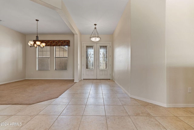 foyer with french doors, a notable chandelier, light tile patterned floors, light colored carpet, and baseboards