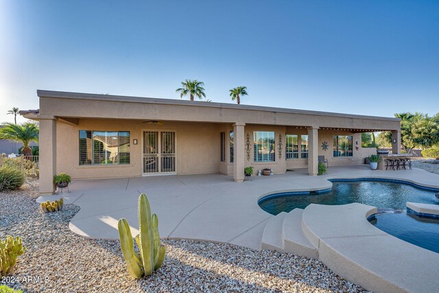 rear view of property featuring a patio, ceiling fan, outdoor dry bar, a pool with connected hot tub, and stucco siding