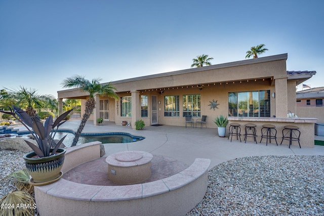 rear view of house with a patio area, an outdoor pool, outdoor dry bar, and stucco siding