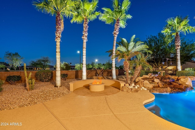 pool at twilight with an outdoor fire pit, a fenced backyard, and a patio