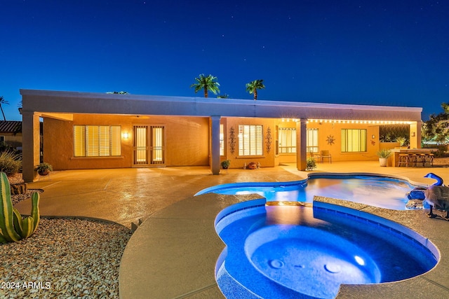 back of house at twilight featuring a patio, a pool with connected hot tub, outdoor dry bar, french doors, and stucco siding