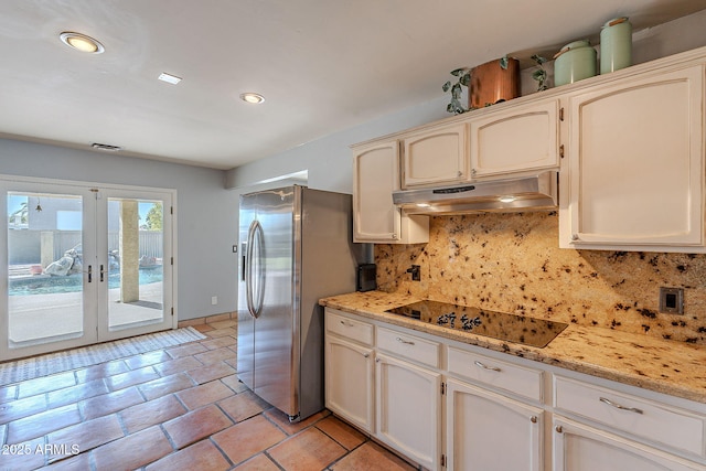 kitchen with light stone counters, backsplash, stainless steel fridge, and black electric cooktop