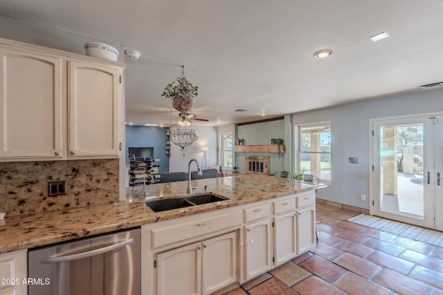 kitchen featuring a fireplace, tasteful backsplash, sink, stainless steel dishwasher, and light stone countertops