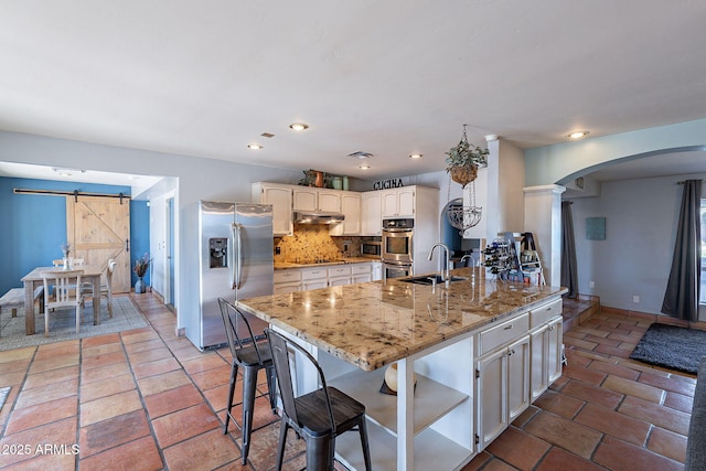 kitchen featuring sink, stainless steel appliances, tasteful backsplash, light stone counters, and a barn door