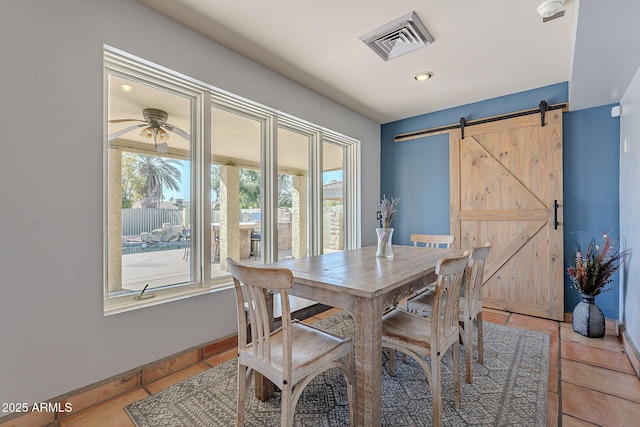 dining room featuring ceiling fan, tile patterned floors, and a barn door