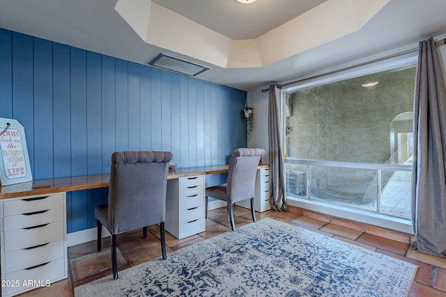 home office with a raised ceiling and wood walls