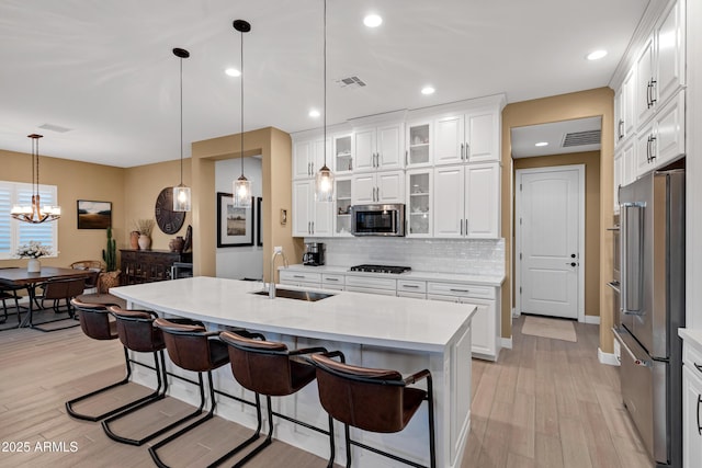 kitchen with white cabinetry, appliances with stainless steel finishes, sink, and a center island with sink