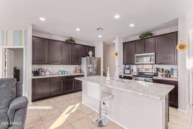 kitchen with a center island with sink, sink, light tile patterned flooring, dark brown cabinetry, and stainless steel appliances