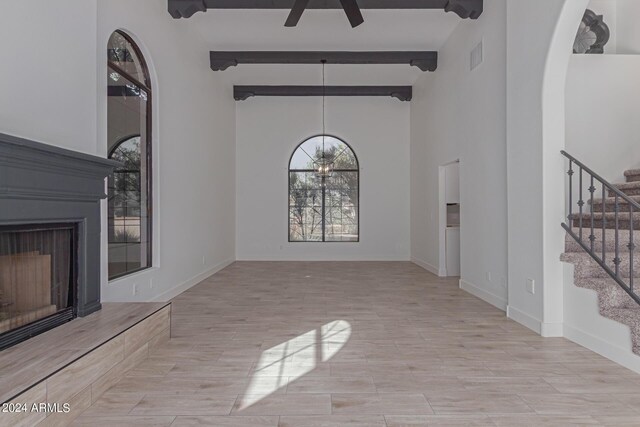 unfurnished living room with a high ceiling, beam ceiling, and ceiling fan