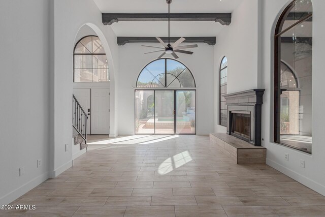 unfurnished living room with a wealth of natural light, ceiling fan, beamed ceiling, and a fireplace